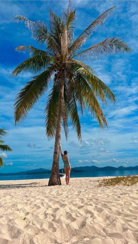 A picture of Beth and a palm tree on Pass Island, Coron, Philippines. Part of a travel guide and travel blog on what to do in the Philippines.