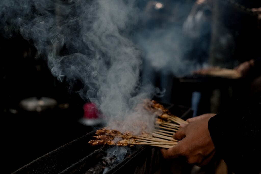 Delicious satay skewers being grilled and smoked in a vibrant street market in West Java, Indonesia.