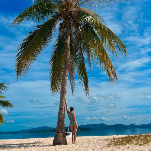 A picture of Beth and a palm tree on Pass Island, Coron, Philippines. Part of a travel guide and travel blog on what to do in the Philippines.